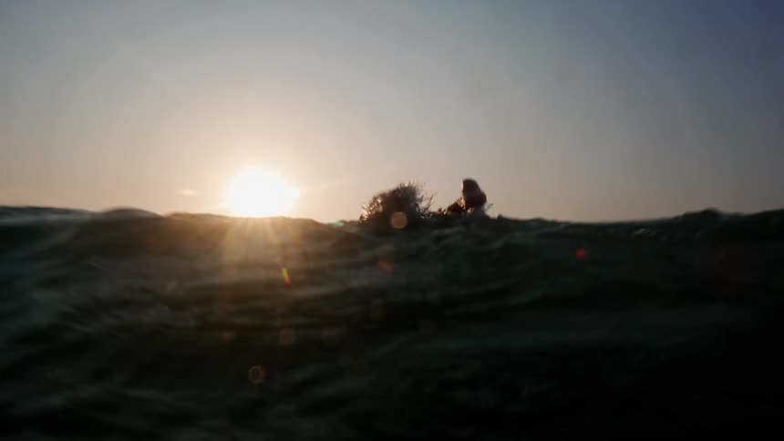 A young woman is surfing on the ocean in the middle of the day