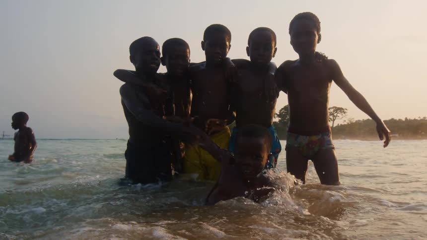Group of children standing on the shallow water in the coast pose for the camera at evening