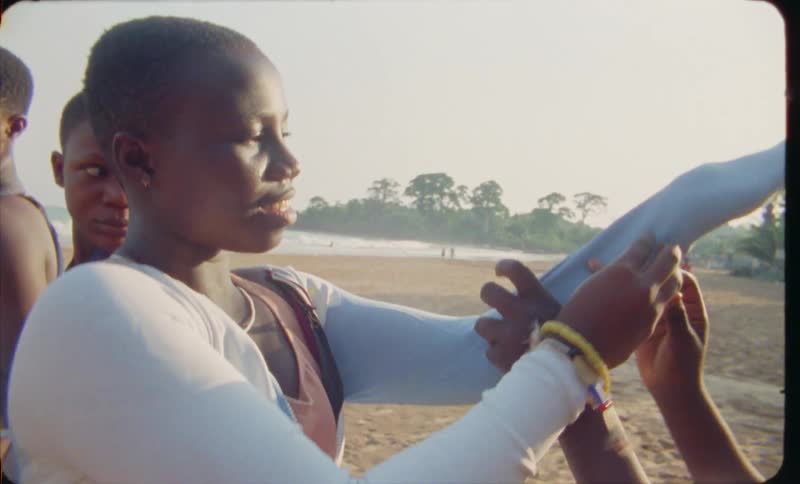 A young girl helps her friend get dressed while standing in the sand on the seashore