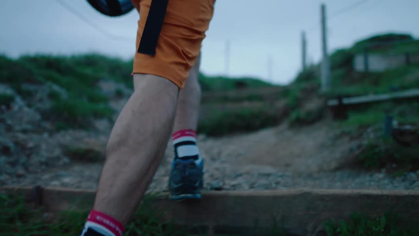Cyclist carries a mountain bike over his shoulders while climbing stairs on a mountain side