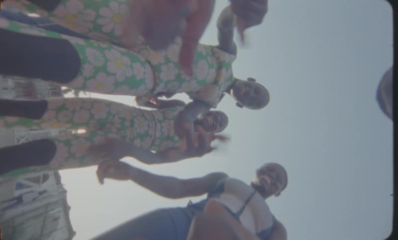 A group of children are standing outside in a circle looking down laughing and waving
