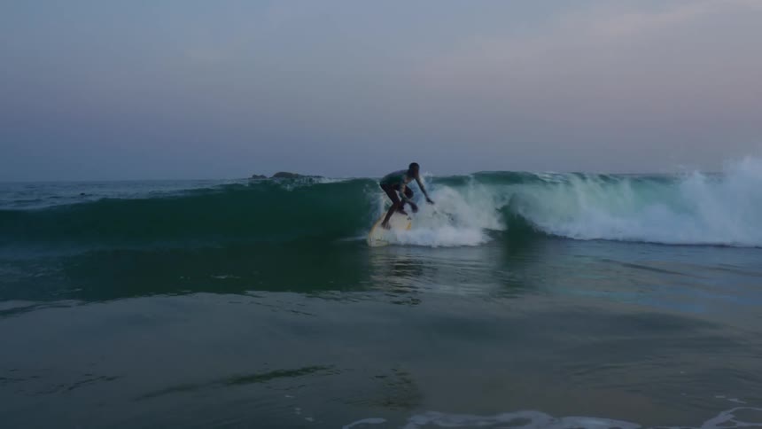 A teenage boy is riding a wave on his surfboard but he falls into the water as he tries to stand