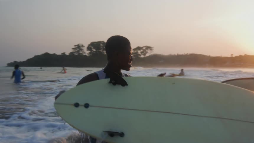 A group of boys in the ocean with surf boards with waves crashing over them