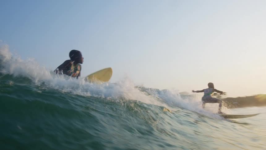 Two boys are on their surfboards riding a wave into shore