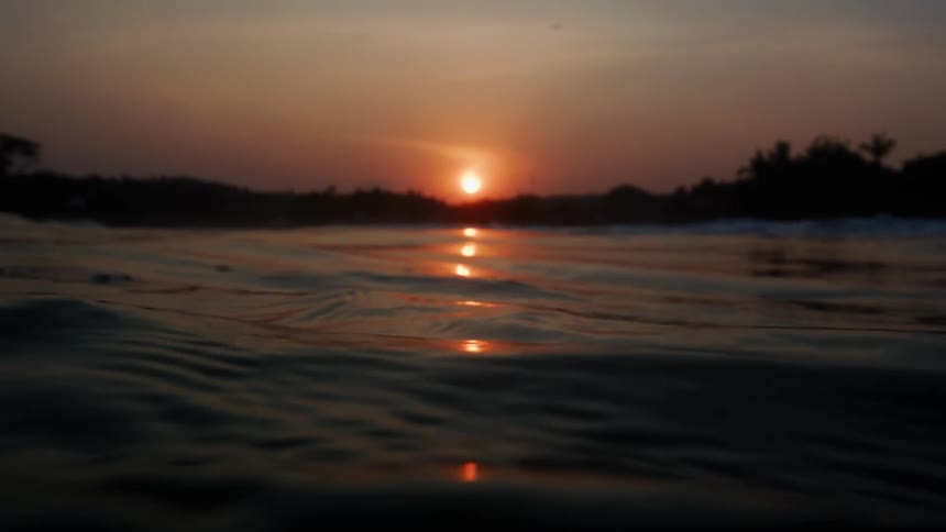 Light shines on the water as it ripples and waves as the sun sets on the horizon