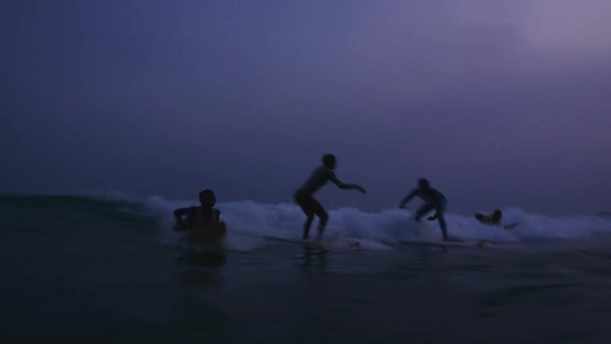 A group of children riding wave on skateboards at dusk