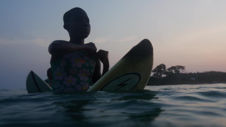 A young teen is sitting on a surf board in the water