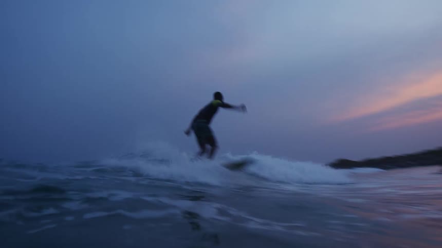 Time lapse footage of a young man riding a surfboard on the waves near the coast at evening