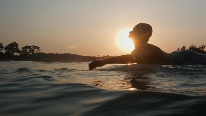 Silhouette of a young woman riding a surfboard on the ocean at sunset