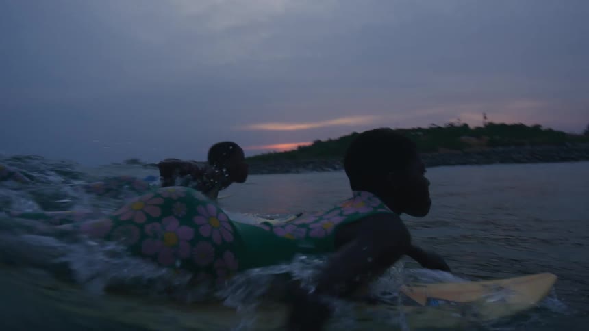 Two black teens paddle toward shore on surfboards