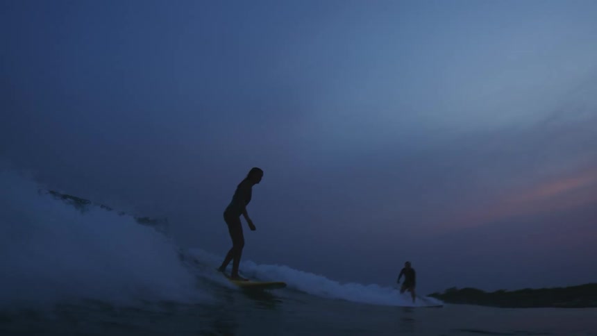 Two people are surfing the waves in an ocean at dusk