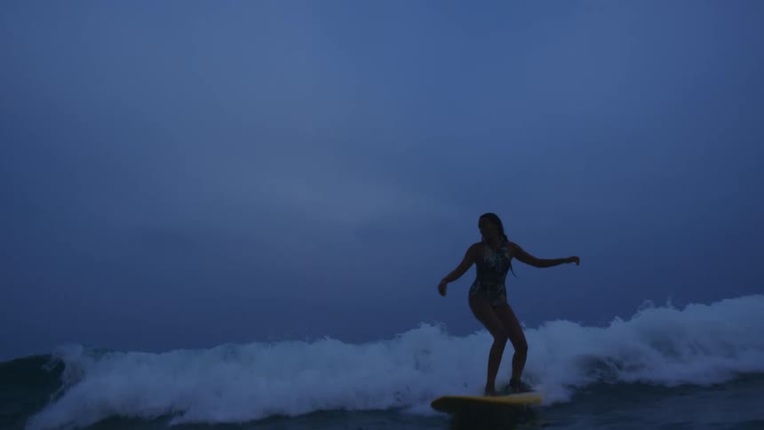 A female is surfing on ocean water during the night