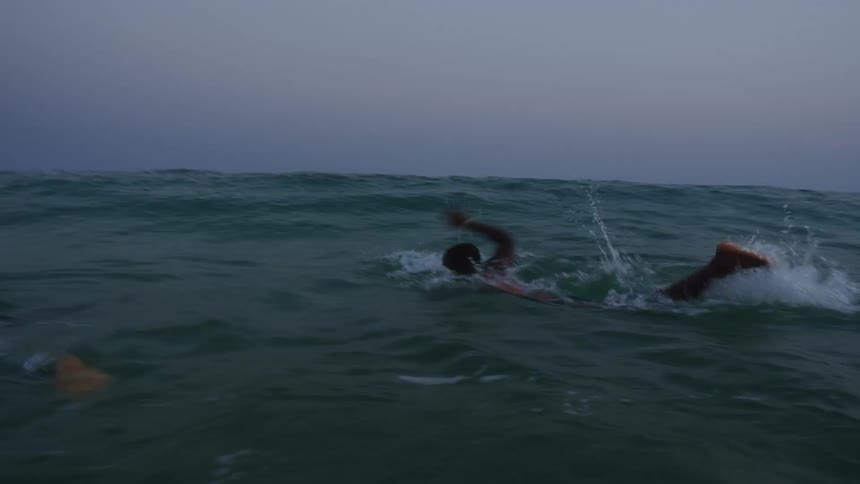 A young woman leaps up in the ocean and begins swimming