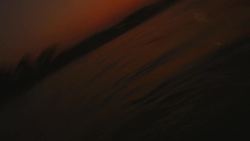 Waves roll toward shore under a dark red horizon at night