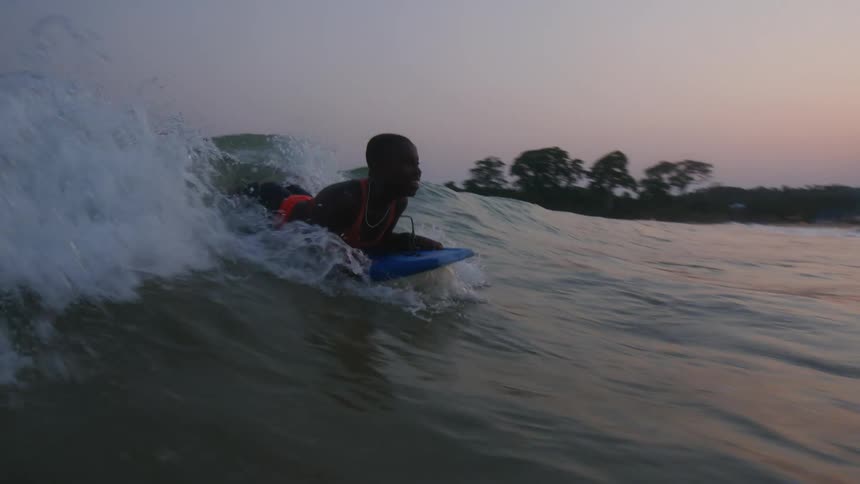 Young woman rides a soft top surfboard on the waves near the coast at evening