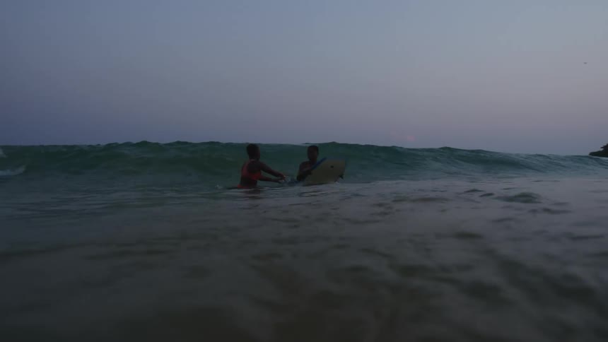 Man on his stomach rides board toward shore as woman moves out to sea