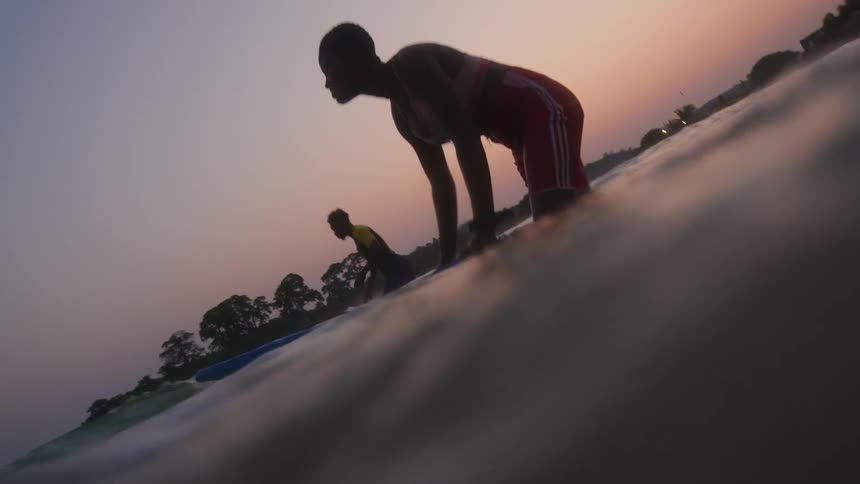A young man and woman lean onto body boards while getting into the ocean