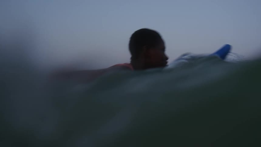 A female is surfing in the ocean water at dusk