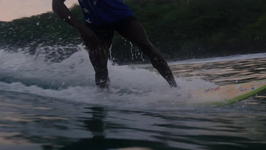 Young man rides a surfboard on the waves near the coast at evening