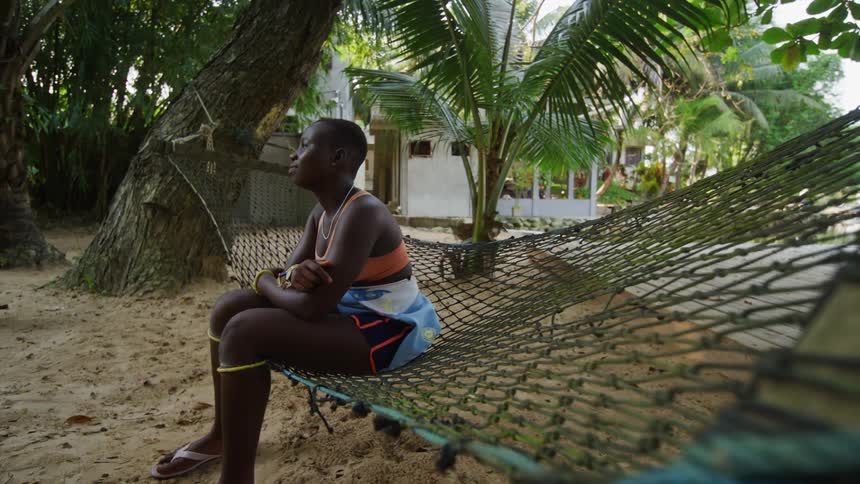 Woman sits in swaying hammock and looks around with white house in the background