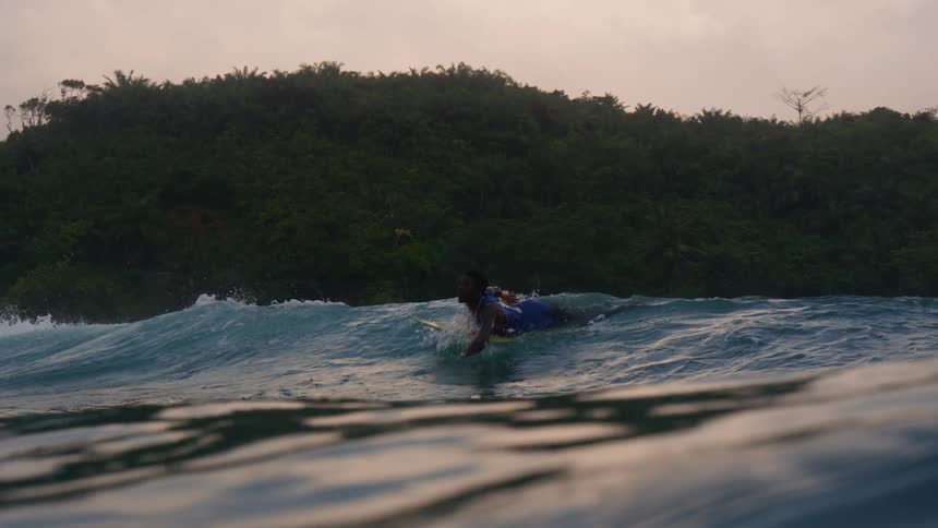 A man laying on a surfboard riding waves as he paddles with his out further into the ocean