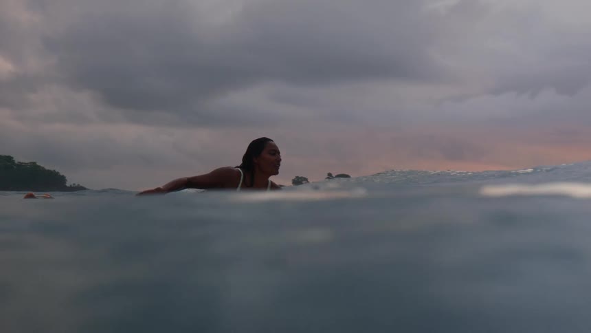 A woman paddles her surfboard in the ocean