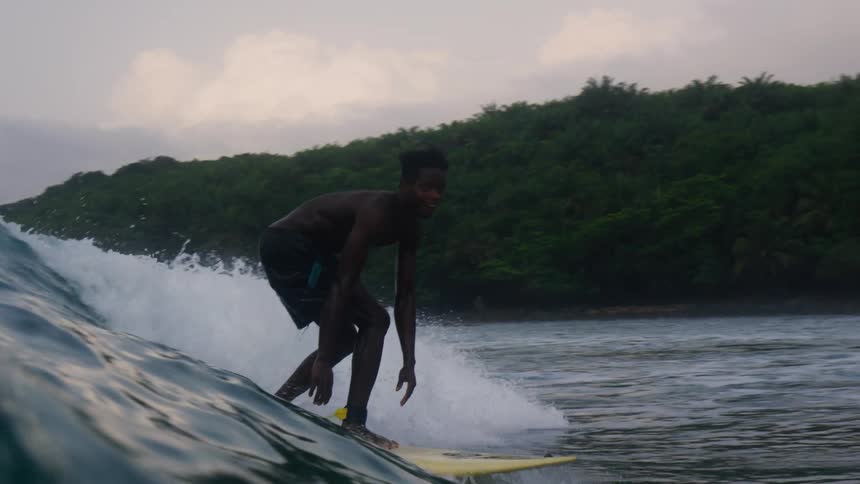 A man bends down on his surfboard as he rides a big wave into shore