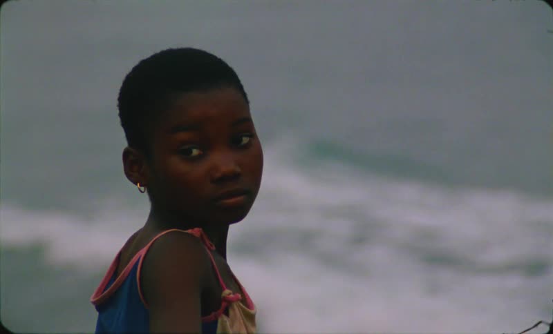 The view is of a young kid that is standing in front of the ocean