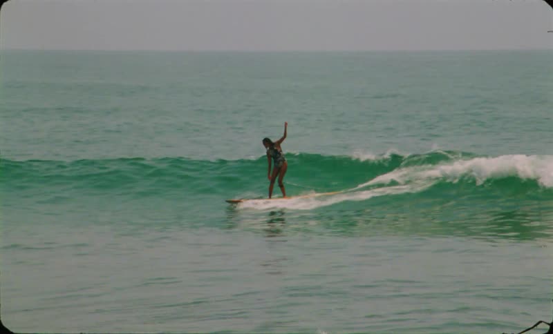 A woman is surfing and she walks on her surfboard as she rides a big wave and falls into the water