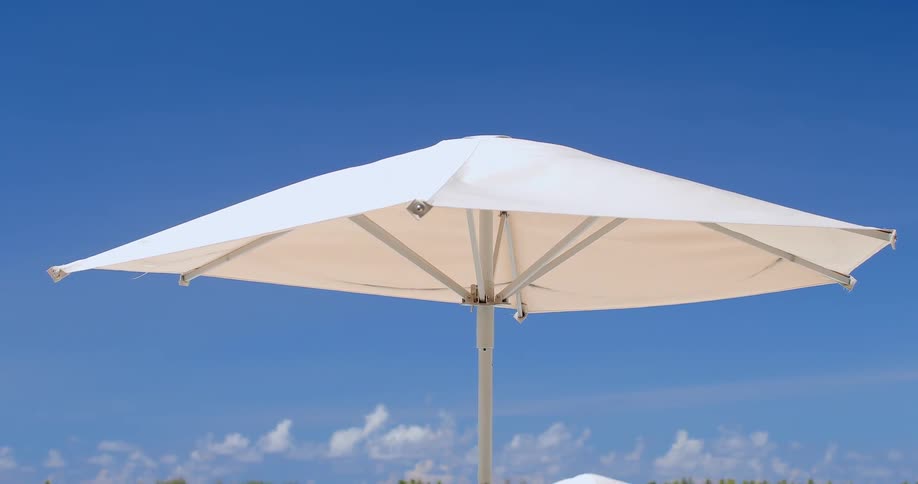 A white beach umbrella sways in the wind