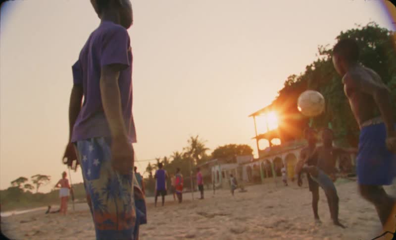 A group of young boys are playing soccer in the sand at sunset