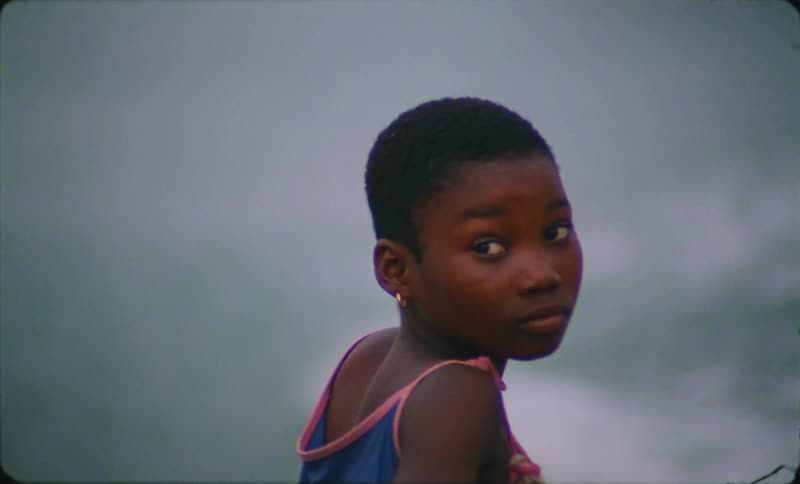 A young girl looks around while standing next to the ocean as waves roll in