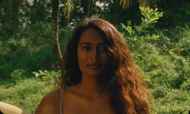 A young woman is looking at the camara and holding a surf board