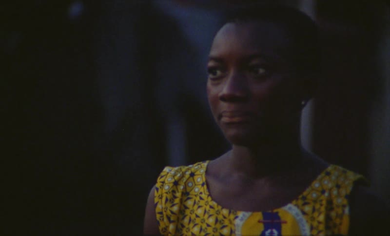 Young woman wearing a bright yellow dress walks on a street at evening