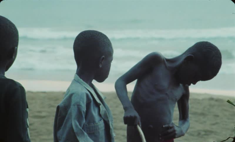 Group of boys hang around on the beach at daytime caught on vintage film