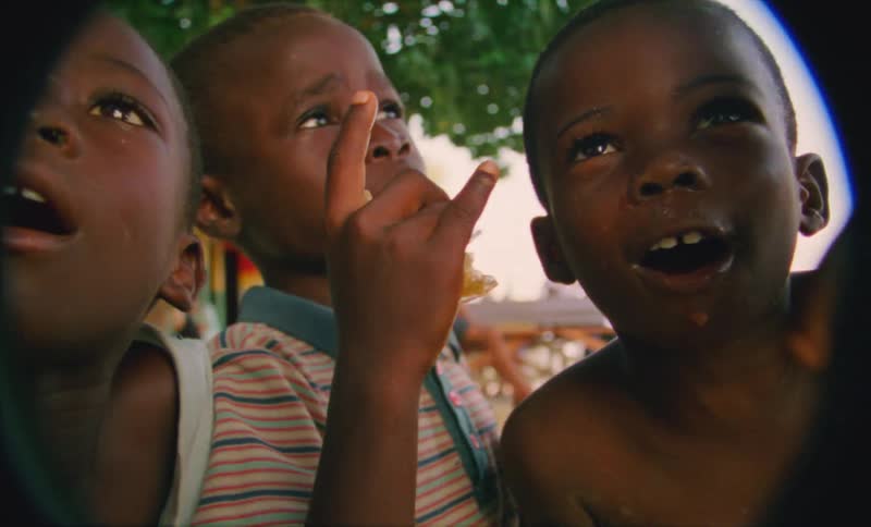 A group of young boys laugh while leaning into a camera lens