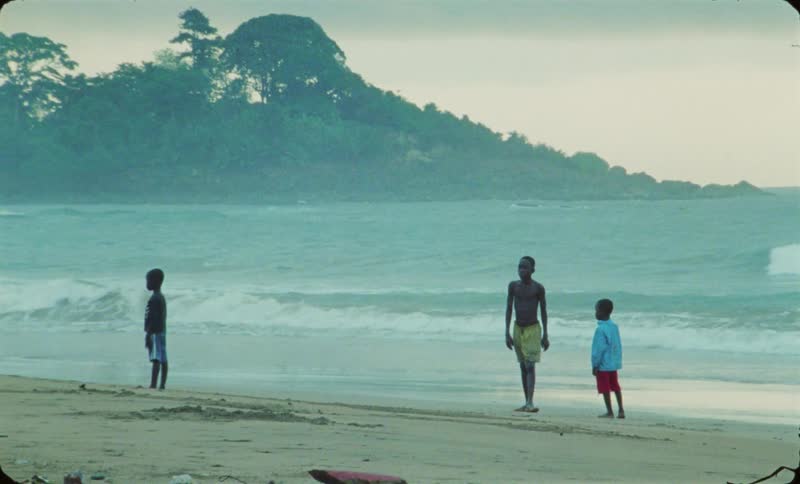 A boy walking on the coastline of a beach kicks a soccer ball at evening