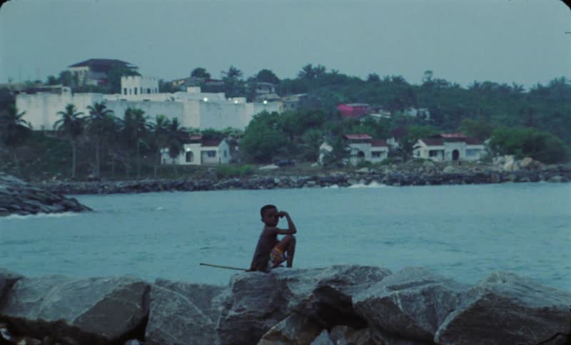 A boy sits on rocks overlooking the ocean