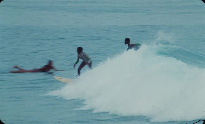 Two women ride surfboards on the ocean waves near the coast caught on vintage film
