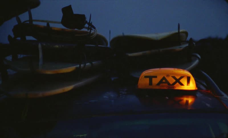 A taxi at nighttime with several surfboards piled on top
