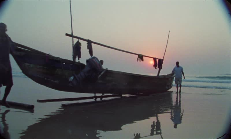 A group of teenage boys move a wooden boat on a beach at sunset next to the ocean