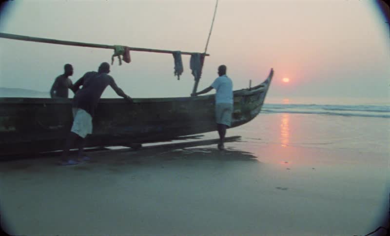 A group of 4 men pushpull a long canoeshaped boat towards the sea the sun is close to the horizon in the background
