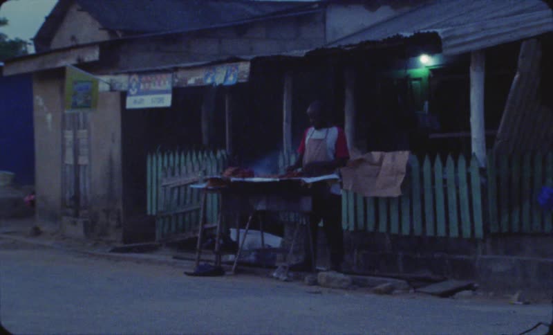 Man stands grilling food for meat sticks between road and building