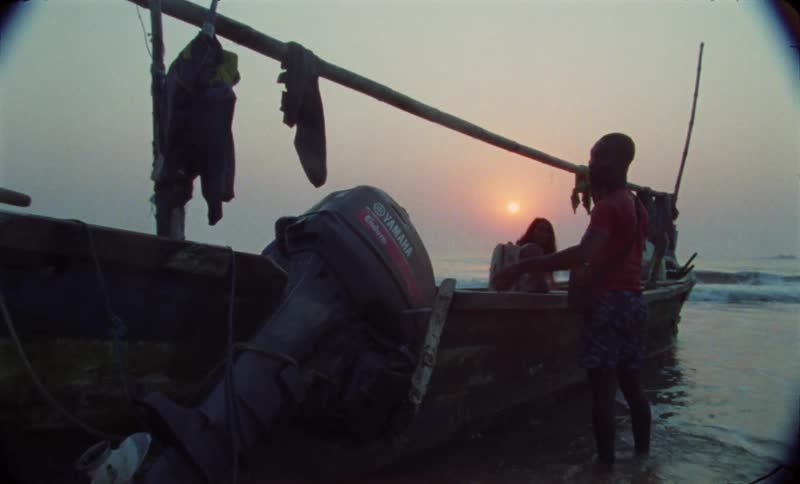 People launch motorboat on coast as waves roll in under a red sky