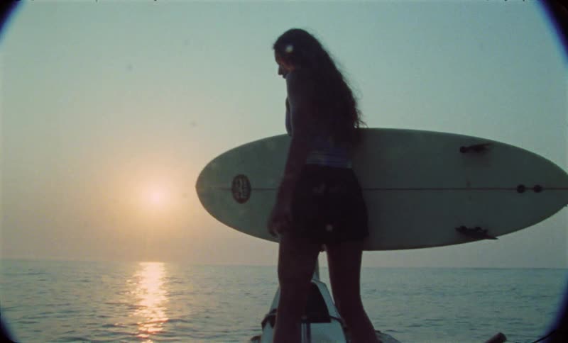 A woman standing holding a surfboard while the platform she stands on bobs around