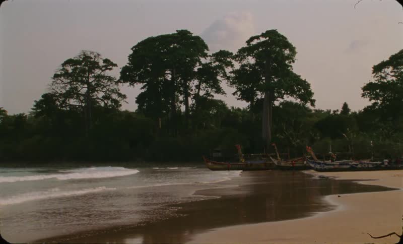 Boats are sitting on the beach as waves roll into shore as a person walks across the sand