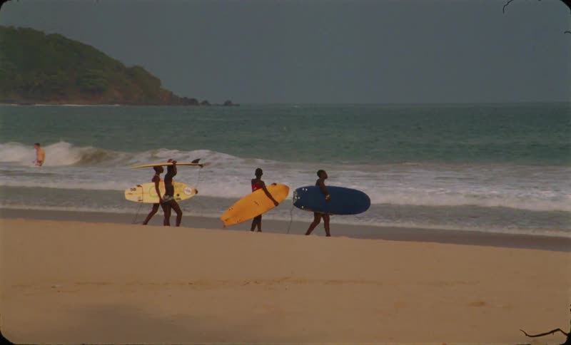 A group of friends carrying surfboards walks into sea