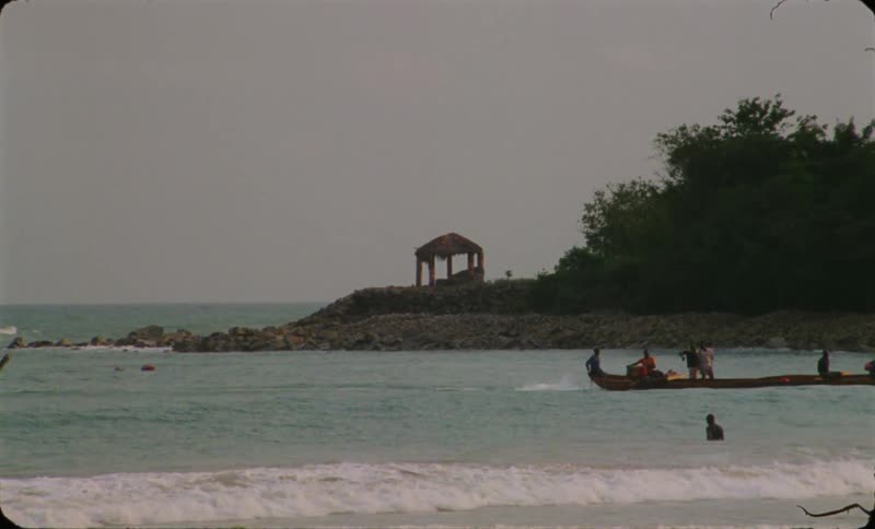 A thing long boat sailing to coast on a tropical beach caught on vintage film