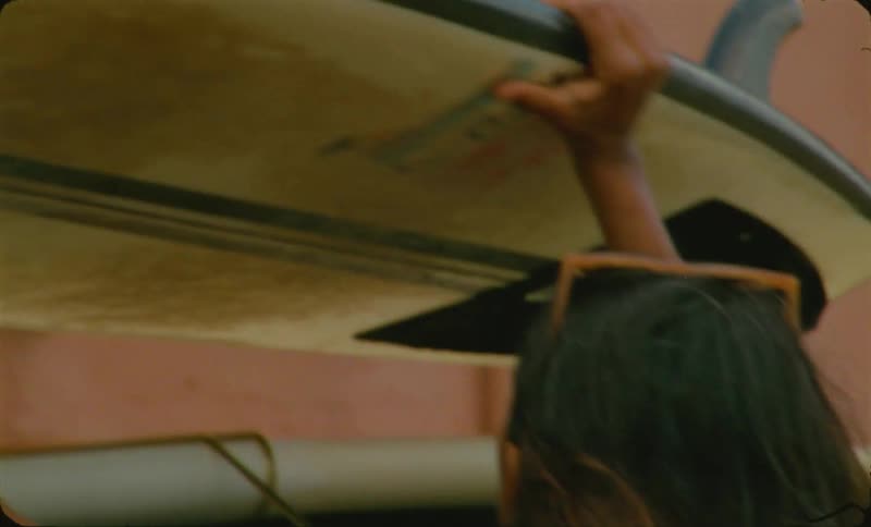 The view is of a woman putting surf board on top of the taxi