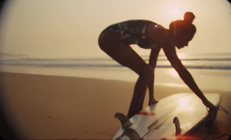 The view is of a young woman walking in the sand with her surf board
